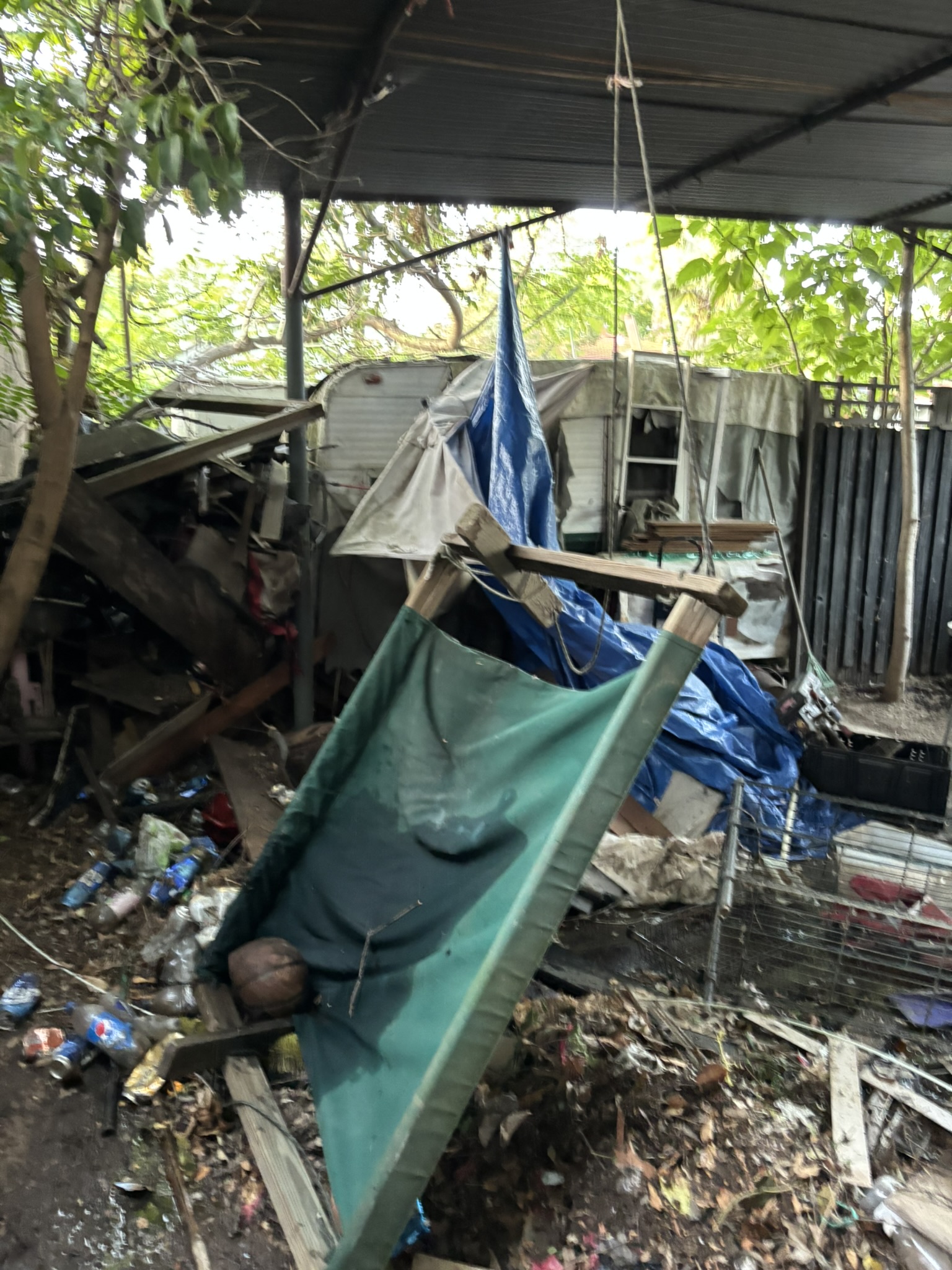 Backyard with collapsed canopy, trailers, and heavy debris — before cleanout